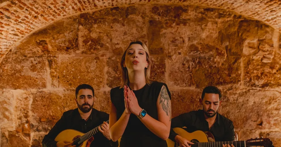 Uma fadista entre dois guitarristas sob uma abóbada de pedra numa pequena casa de fado