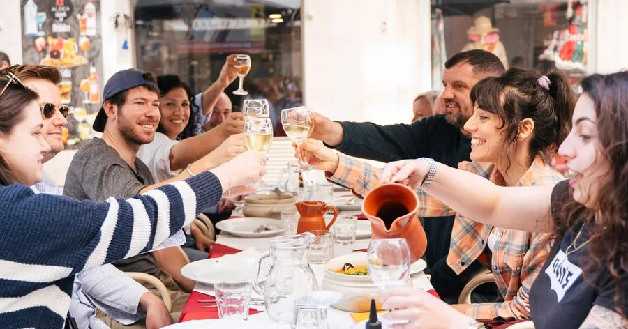 Um grupo a erguer copos de vinho branco sobre pratos numa mesa movimentada de restaurante